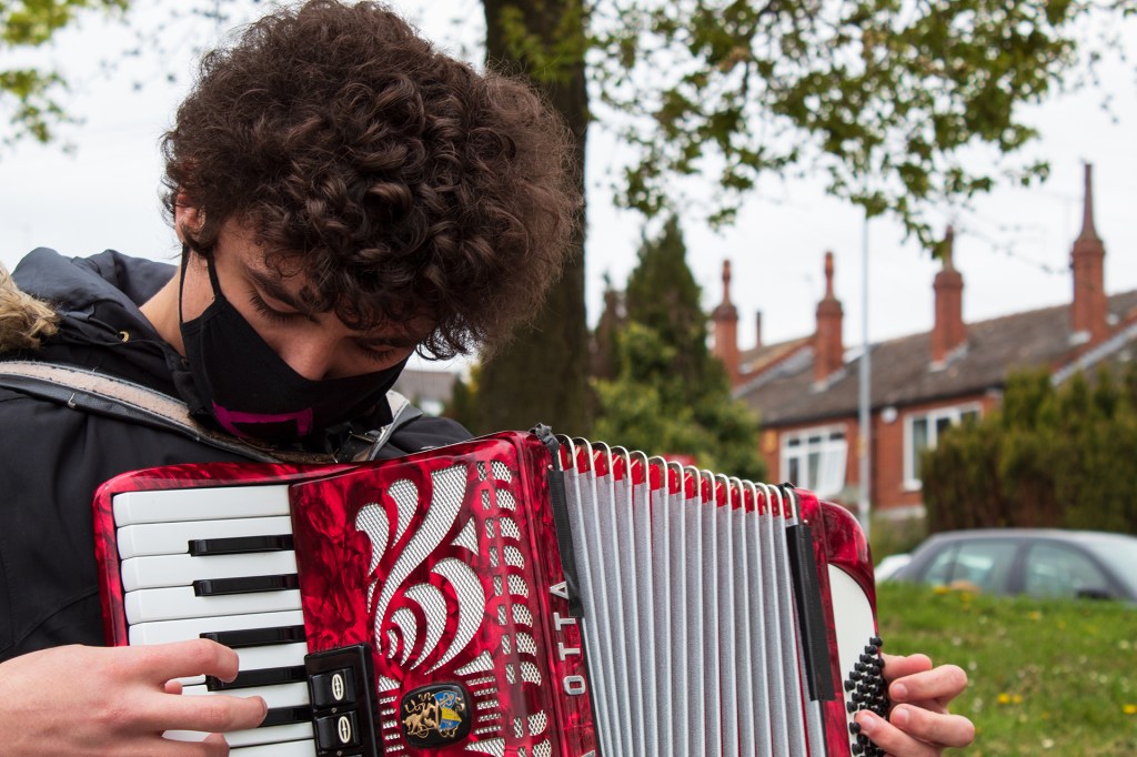 Jordan looking down as he plays his red accordion with it's white flowing patterned engravings.