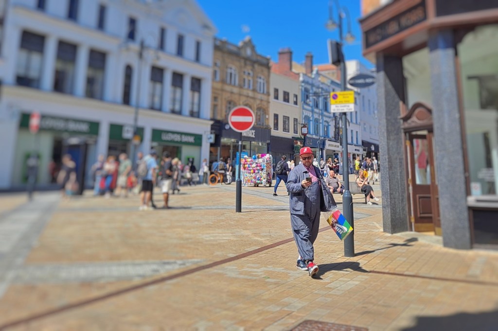 a man walks towards the camera wearing a red hat and looking his phone