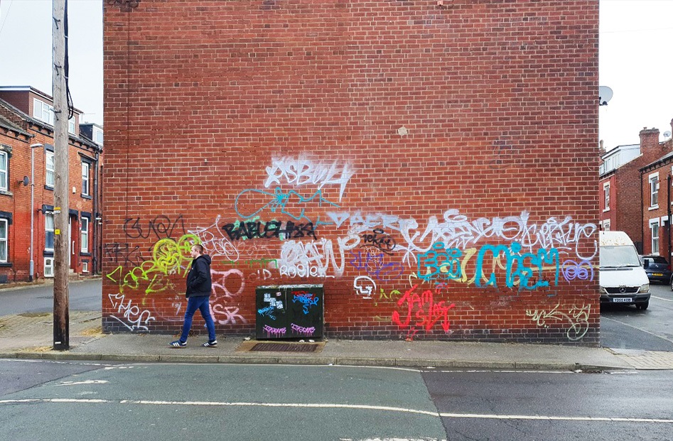 A wall covered in graffiti tags on a busy street in Hyde Park