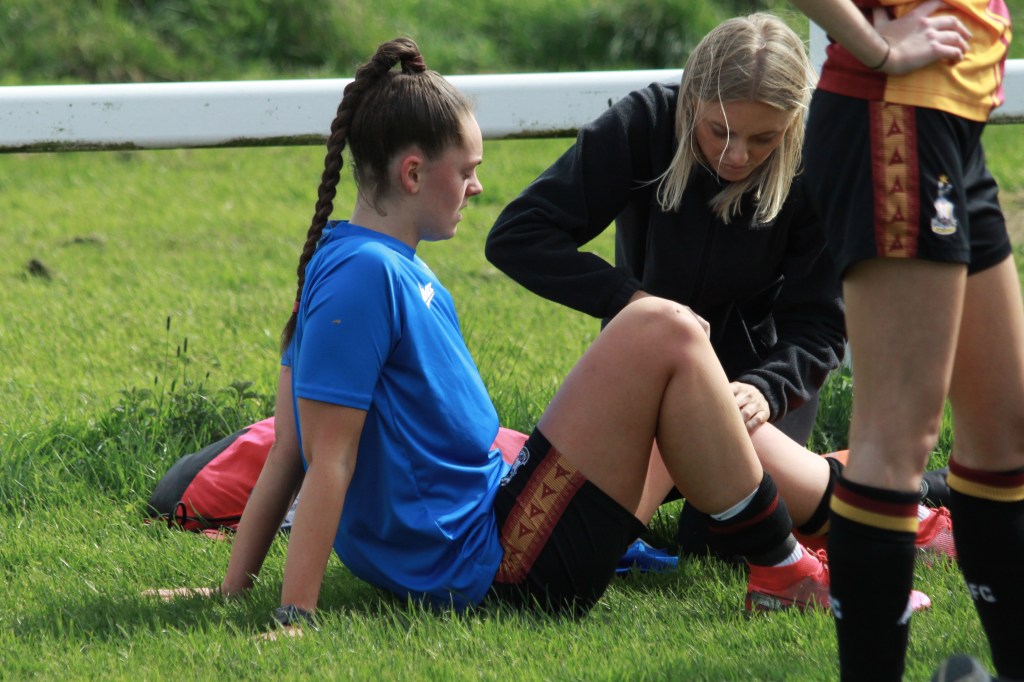 Ash is sat on the floor whilst a physio massages her leg