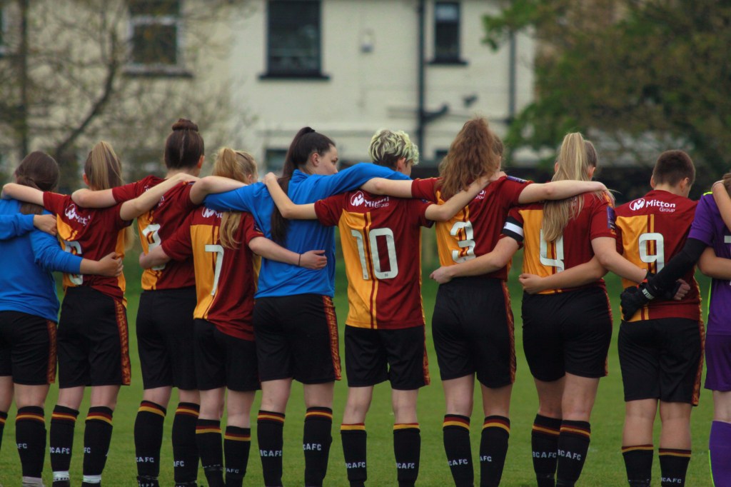 The Bradford city women's U23's wrap their arms around each other in silence. They are wearing their claret and amber kits 