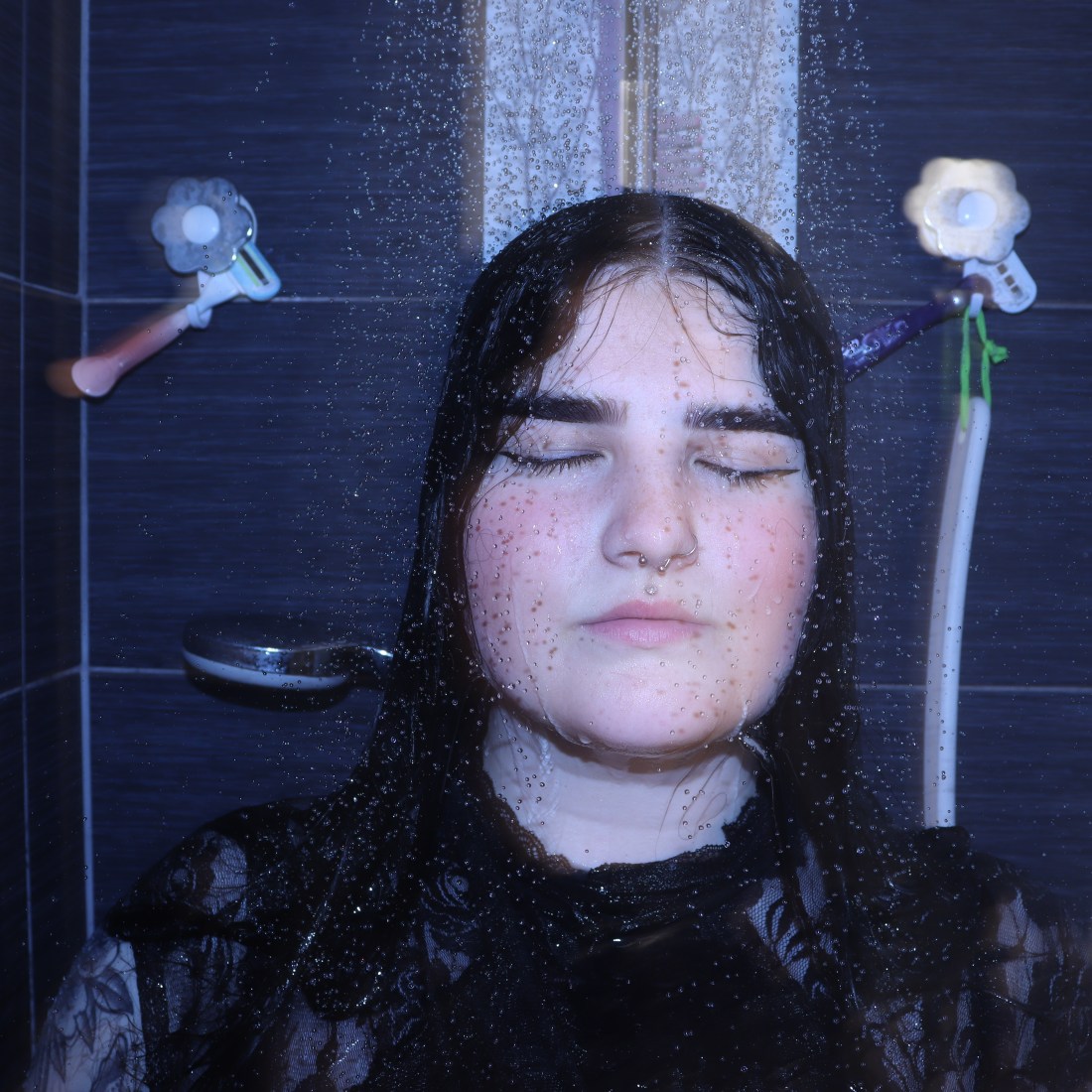 An image of a girl in the shower with makeup on and facial piercings as shower water comes down around her.