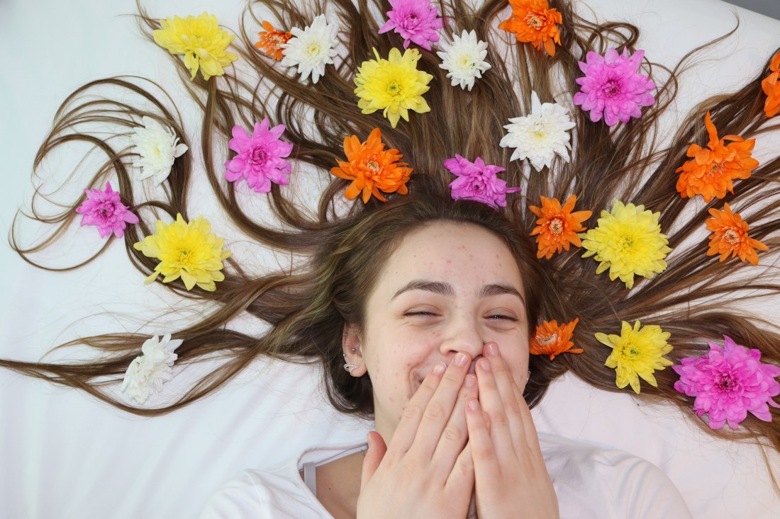 An image of a girl lying in bed laughing with her hands over her mouth and flowers in her hair.