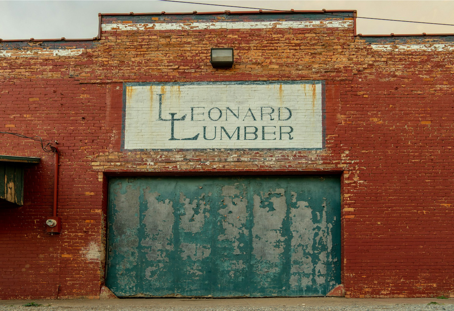 Front of a red brick building with Leonard Lumber in above a green, weathered door.