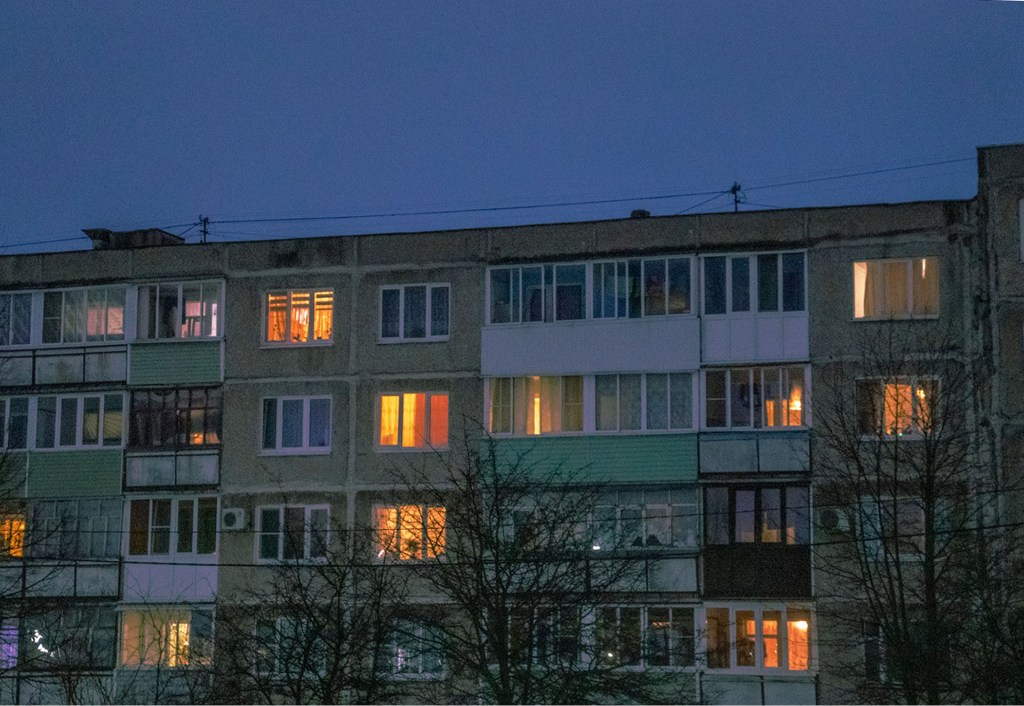 A block of flats that appears run down with some rooms having lights on and some with their lights off.