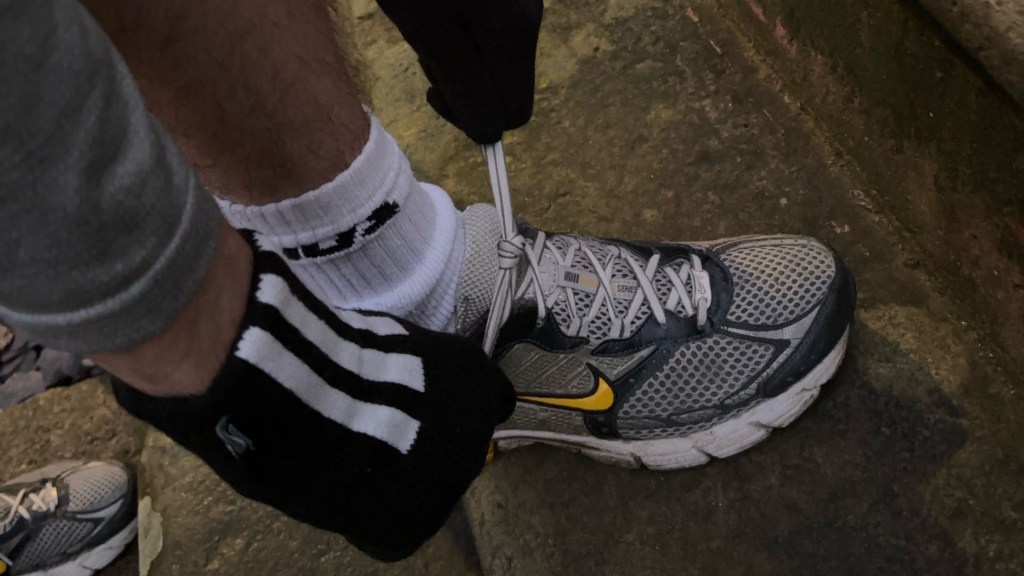 A Nike running shoe up-close and someone with gloves on tying their laces.