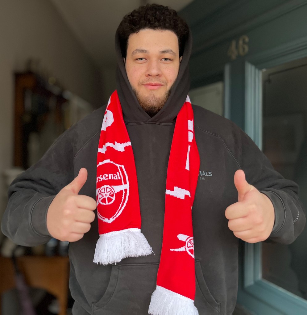 Benjamin Adebiyi, the focus of this piece, in his door, with his thumbs up and an Arsenal scarf on too. 