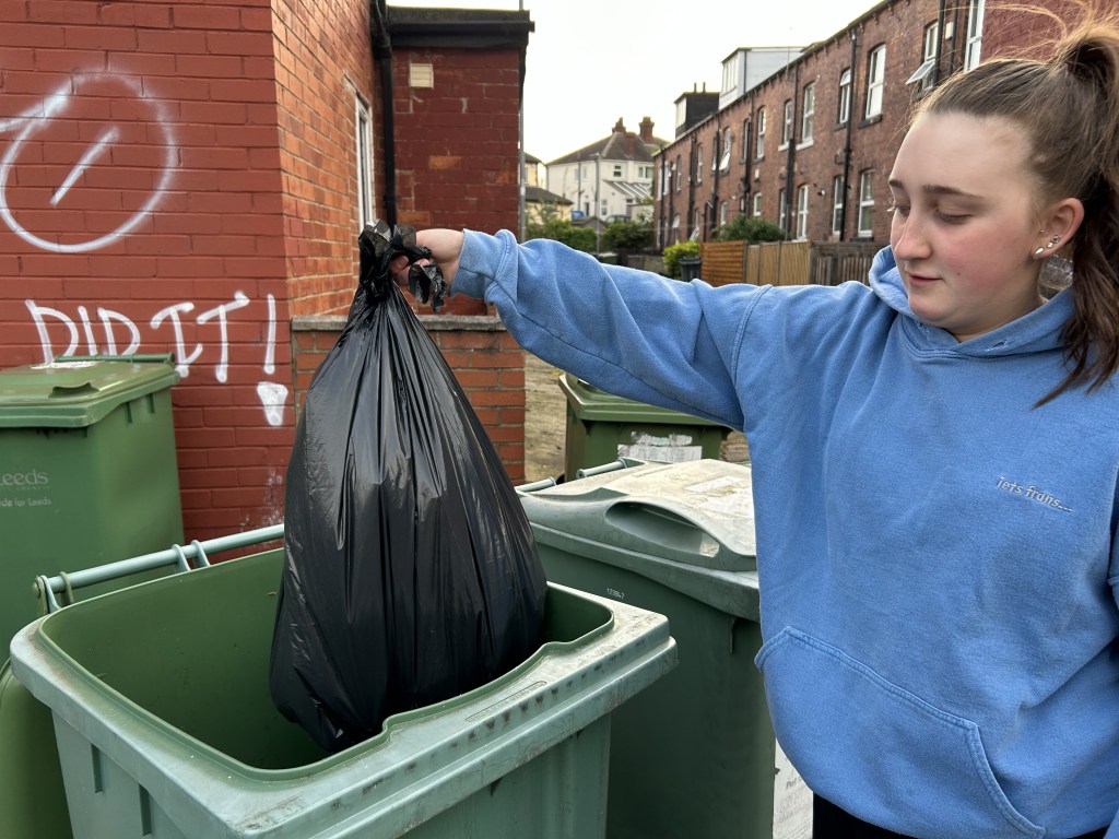 Person putting bag of rubbish inside a bin.