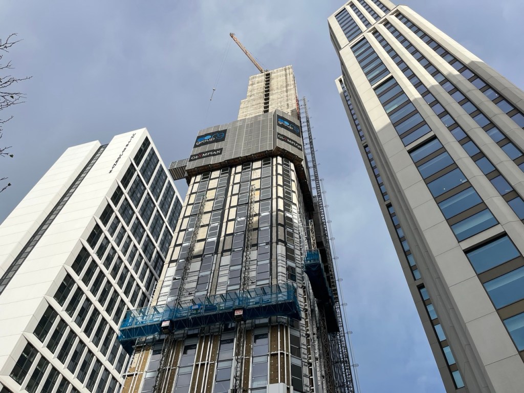 Tower block under construction with blue sky in the background, perspective from street level