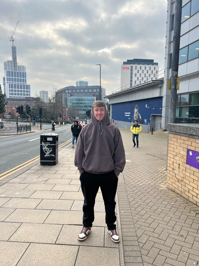 A photo of a person named Ben with a sharp focus on both the subject and the background, taken with an F-stop of 16. The landscape behind him is now more in focus, with less background blur compared to the previous image. The image is bright due to natural light, but the smaller aperture results in less light entering the lens