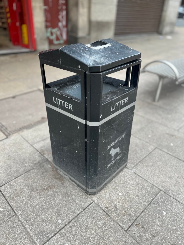 A bin with a bench and the backdoor of a shop in the background