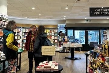A trio of people stood chatting inside of the book shop. 