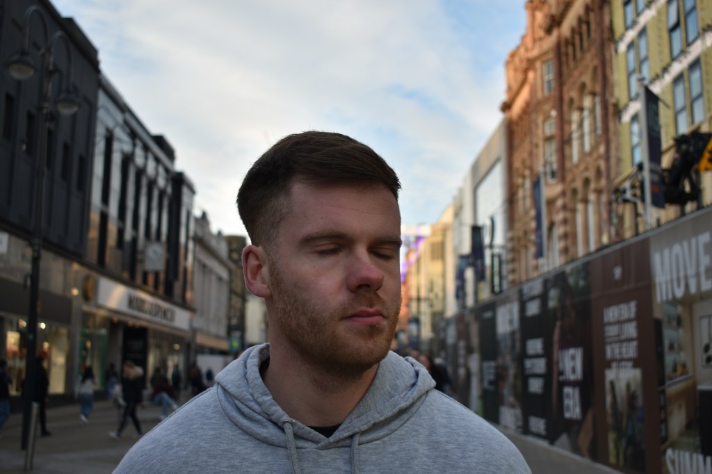 A man on a busy shopping strip, with his head in motion, captured with a slow shutter speed. The background is blurred, and his facial features appear slightly distorted due to the motion blur