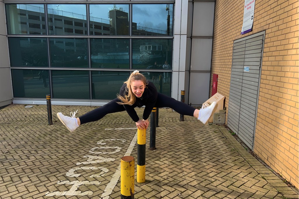 A girl is jumping with her legs out to the side over a black and yellow bollard
