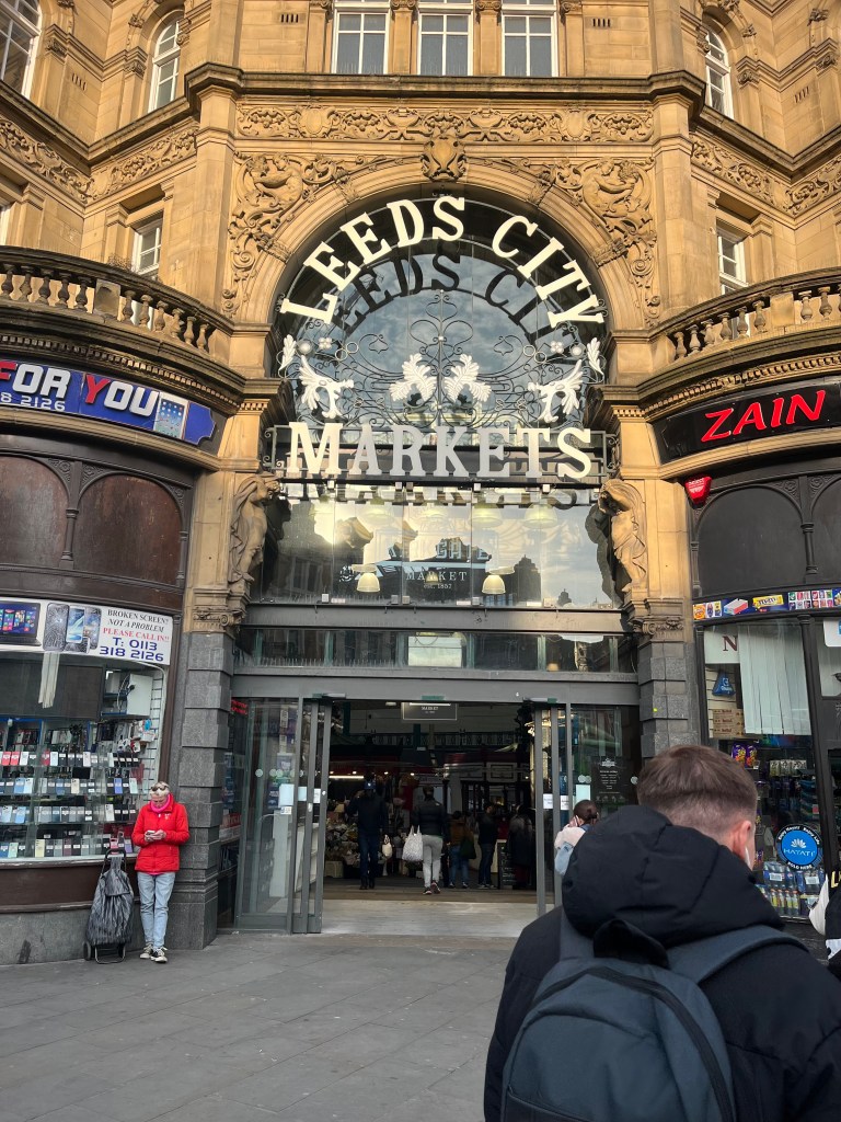 The main entrance of Kirkgate Market in Leeds, featuring large glass doors framed by intricate ironwork