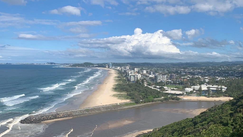 Photo of Sunshine Coast beach from a lookout spot with buildings, ocean and walkway all in the image. Aspect ratio of 16:9 in landscape. 