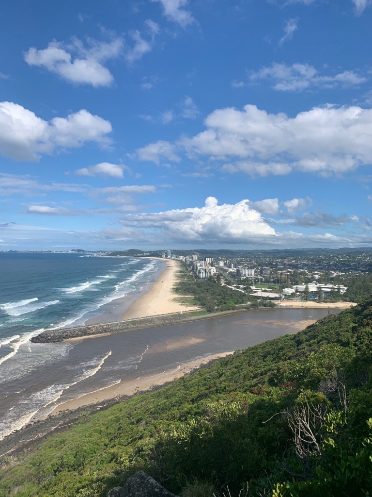 Photo of Sunshine Coast beach from a lookout spot with buildings, ocean and walkway all in the image. 