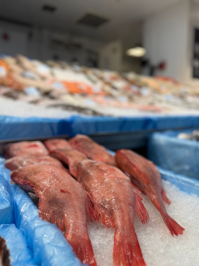 A close-up of red fish on ice, with a blurred background showing more fish displayed on ice at Kirkgate Market