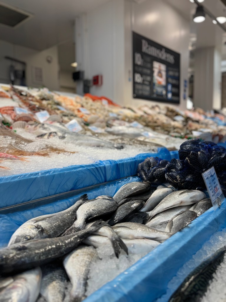 A close-up of mackerel on ice, with a blurred background showing more fish displayed at Kirkgate Market