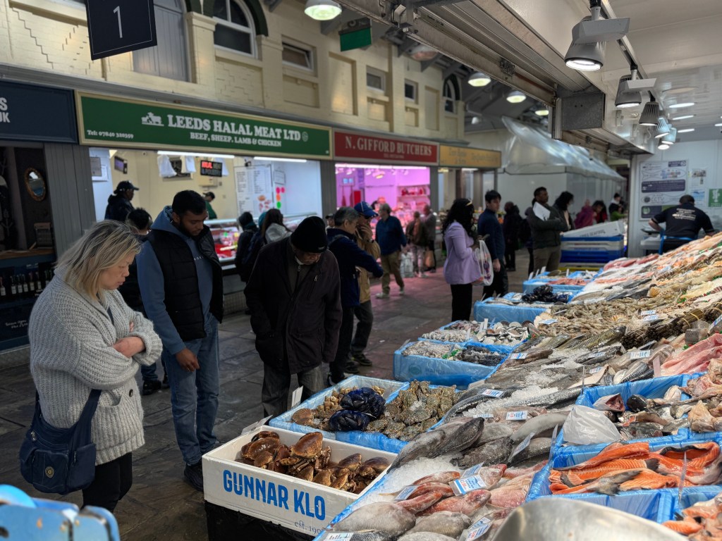 A group of people look at a display of fish at Kirkgate Market, with a couple of butcher shops softly blurred in the background