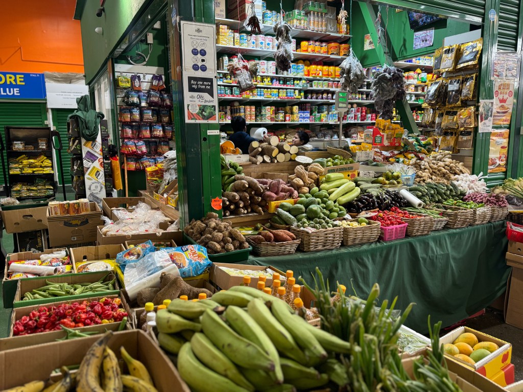 A stall at Kirkgate Market displaying exotic vegetables like plantains, with shelves stacked with products visible in the background