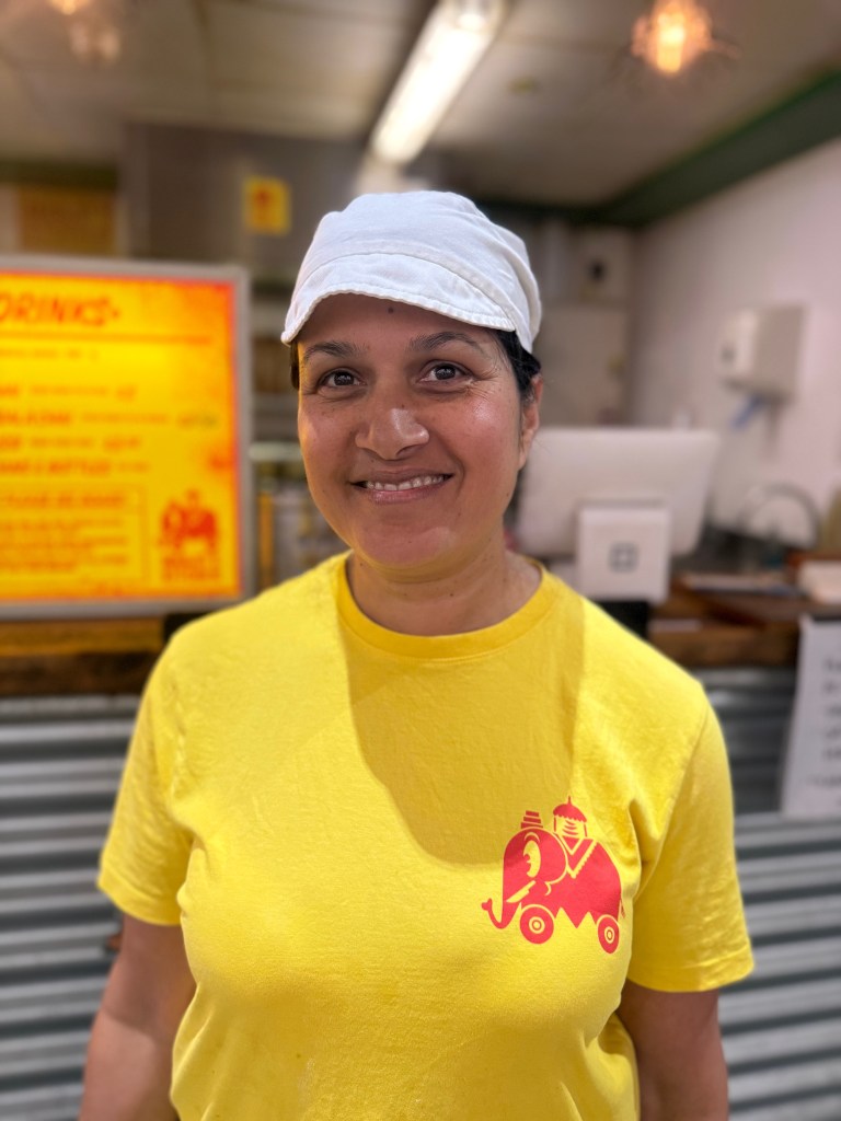 Manjit Kaur stands smiling at the camera outside her food stall, Manjit’s Kitchen, in Kirkgate Market, Leeds