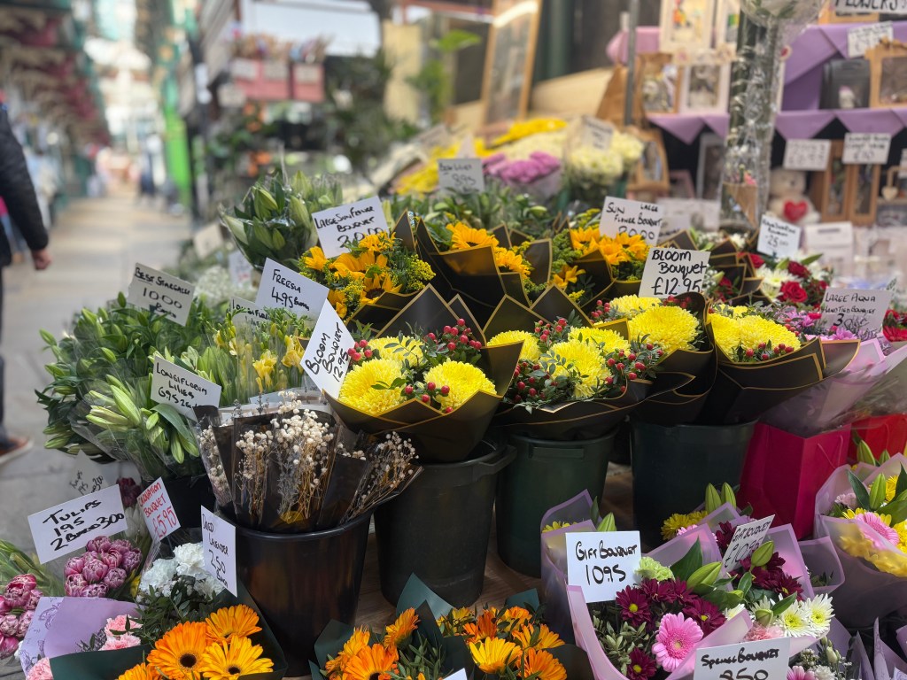 A close-up of a vibrant flower display in Kirkgate Market, with various colourful flowers in sharp focus and a blurred walkway in the background