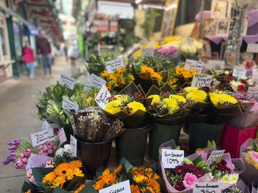 A close-up of a vibrant flower display in Kirkgate Market, with various colourful flowers in sharp focus and a blurred walkway in the background