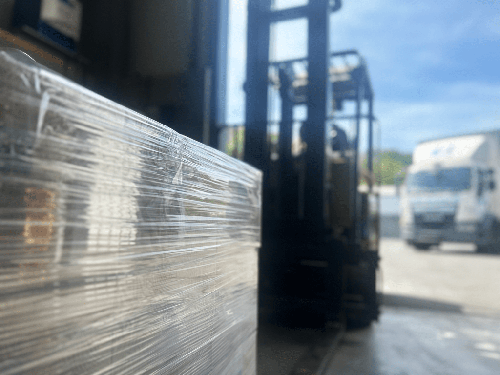A forklift moves in to lift a stack of coffee boxes for loading onto a wagon, which is in the background