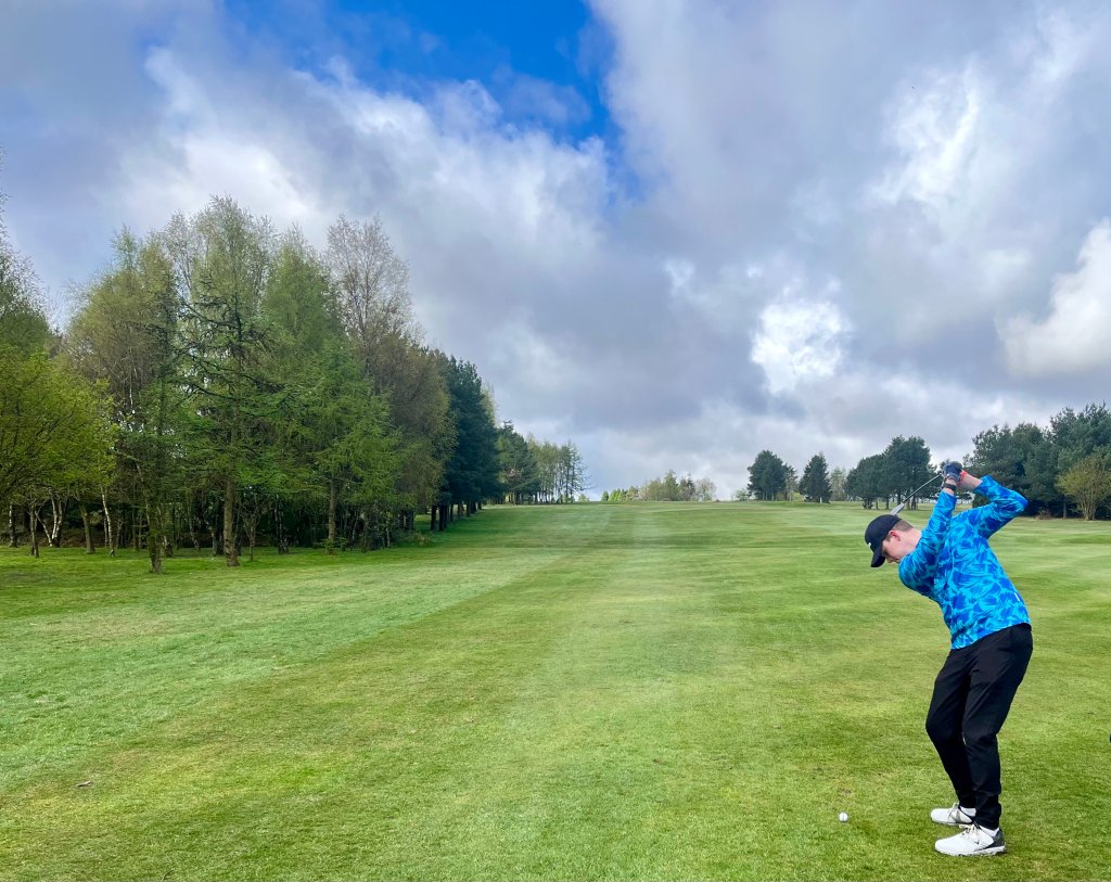A golfer taking a long iron into the green