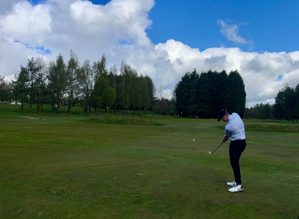 Golfer with pitching wedge in hand and ball in flight