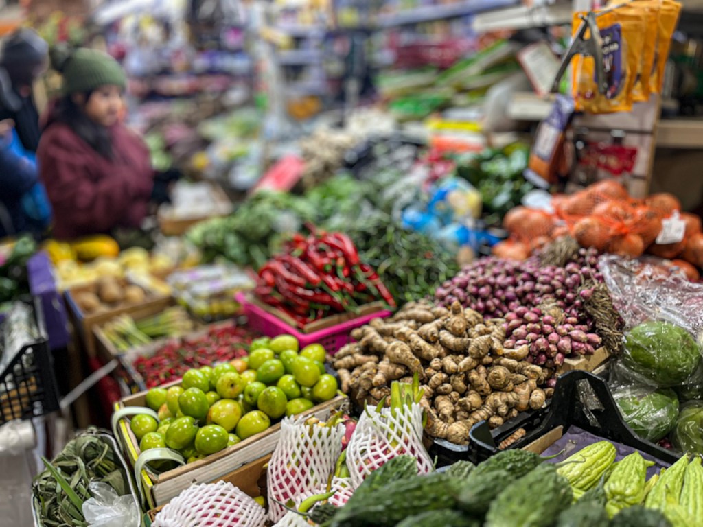 A vibrant market stall displaying fresh vegetables, with people browsing in the background