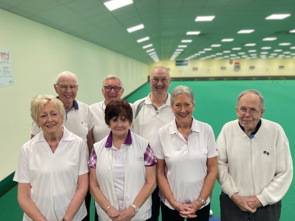A picture of 7 people aged 70 and older standing for a group photo all looking at the camera and smiling