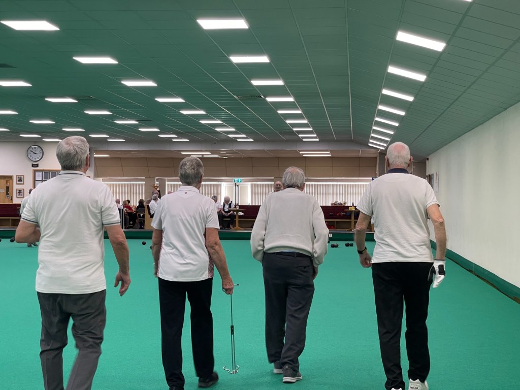 four bowls player walking away from the camera down the green in a line.