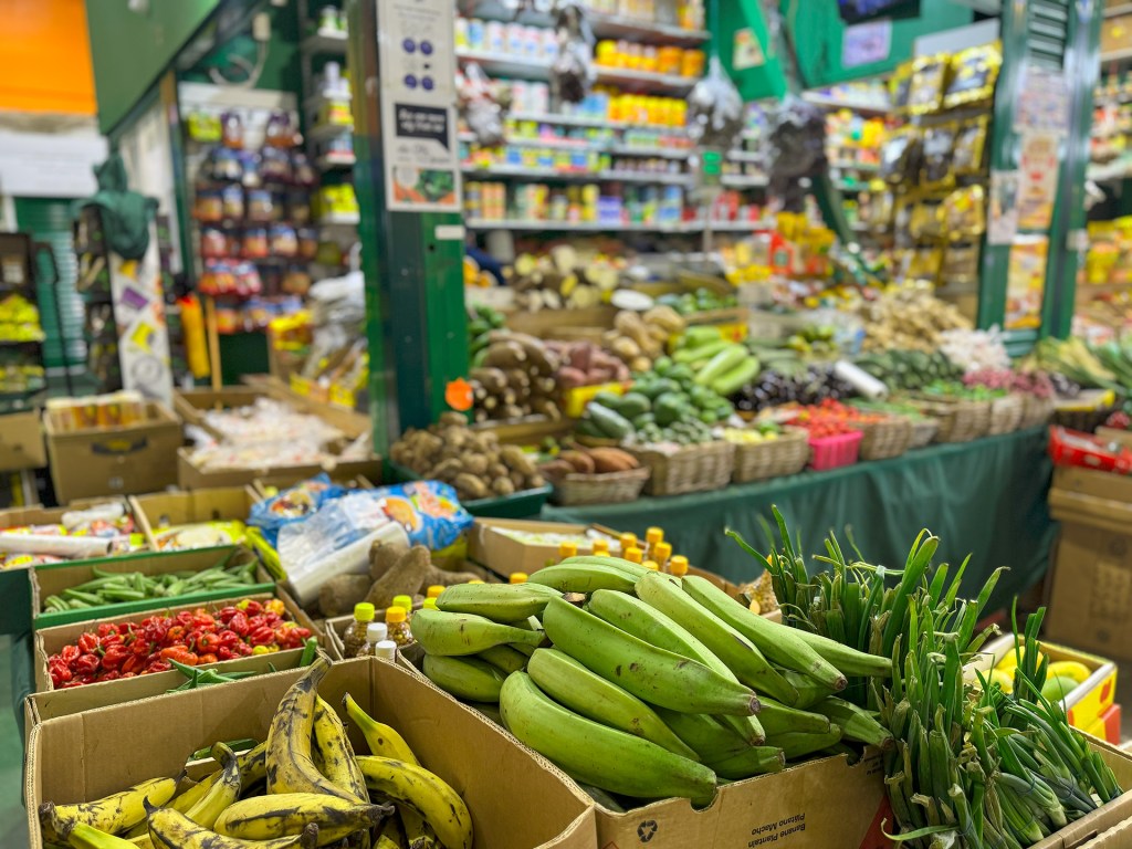 A stall at Kirkgate Market displaying exotic vegetables like plantains, with shelves stacked with products visible in the background